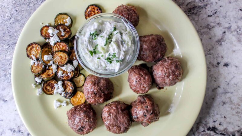 Lamb Meatballs topped with zingy tzatziki sauce, alongside roasted zucchini tossed in lemon and paprika. Easy make-ahead Greek inspired meal!